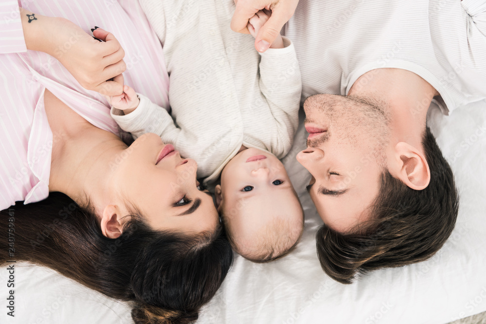 overhead view of happy family with little baby lying on bed together overhead view of happy family with little baby lying on bed together