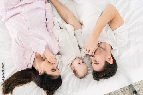 overhead view of happy family with little baby lying on bed together