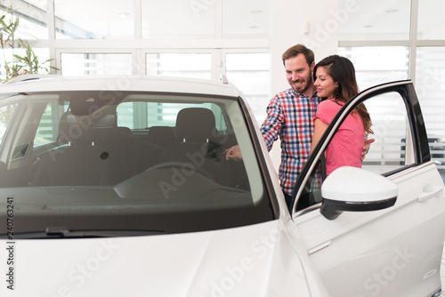 Happy beautiful young couple smiling and buying a car in salon. Man smiling holding keys to his new car. Buying car on credit. Bank credit concept.