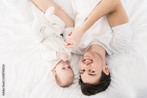 overhead view of smiling father and little baby lying on bed together at home