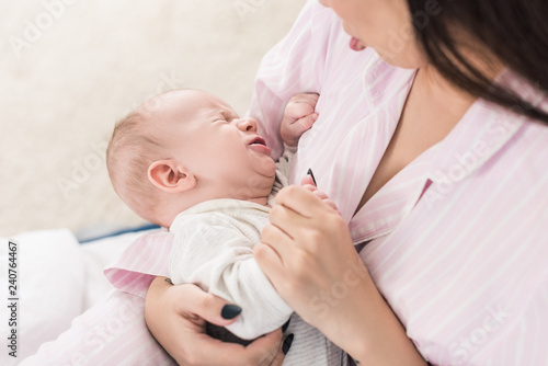 partial view of mother calming down little crying baby on hands