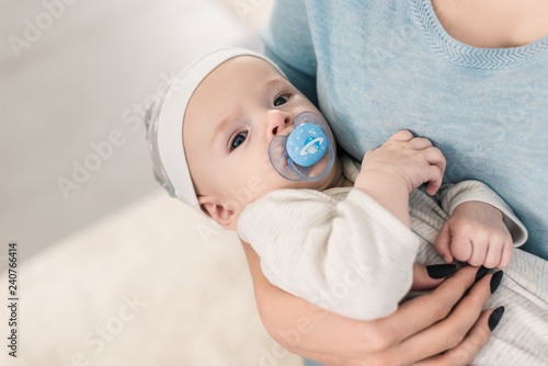 cropped shot of mother holding little son with pacifier in hands photo