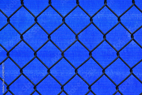 Abstract blue mesh tarp behind a black chin link border fence background