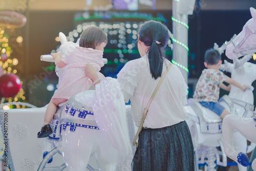 Adorable Asian little kid girl riding on a merry go round carous photo