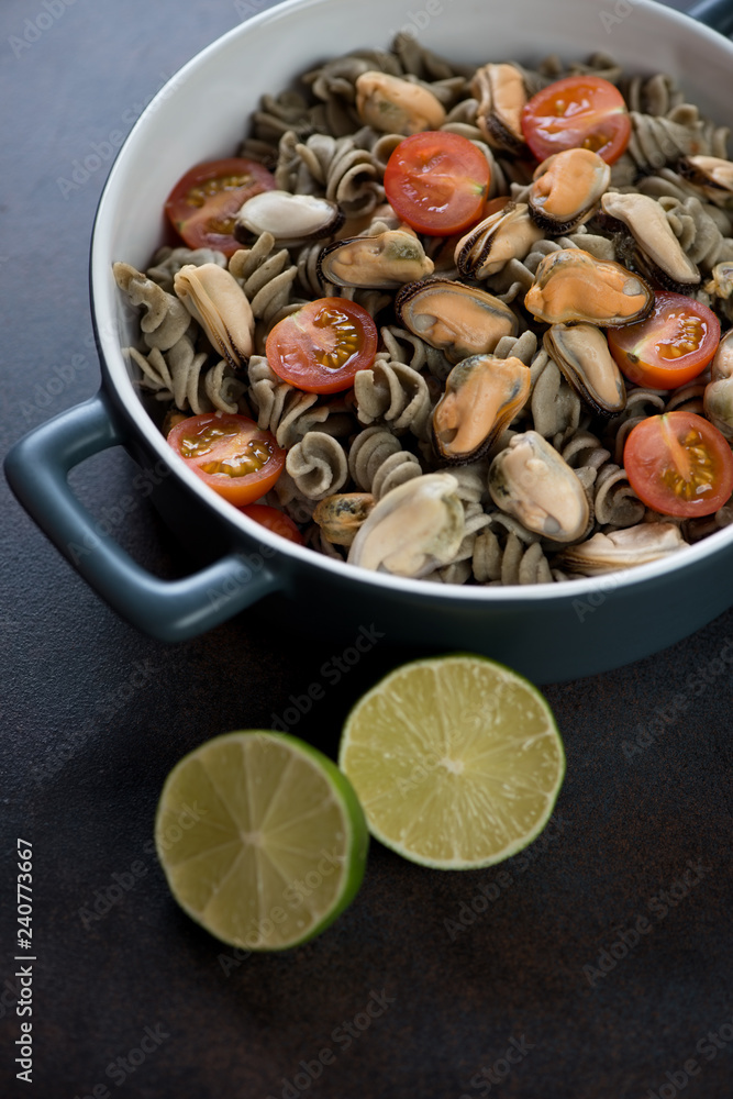 Hemp flour pasta served with mussels and cherry tomatoes, vertical shot on a dark brown metal surface Hemp flour pasta served with mussels and cherry tomatoes, vertical shot on a dark brown metal surface