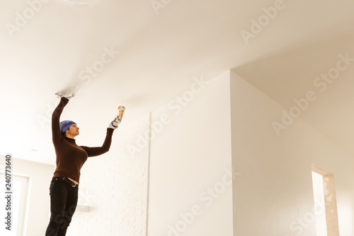 Woman paints ceiling with brush at home