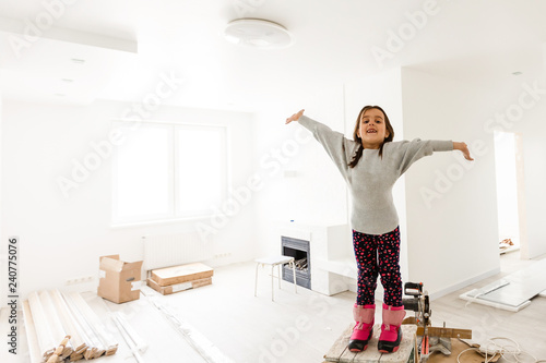 Little girl in pink stands on ladder with ape rule in repaired apartment