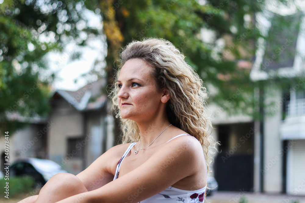 Attractive Blonde Girl With Curly Hair Sitting on the Bench in a Park and Looking Far While Waiting For Someone to Come Attractive Blonde Girl With Curly Hair Sitting on the Bench in a Park and Looking Far While Waiting For Someone to Come