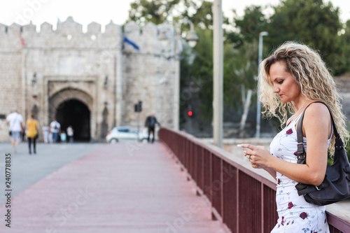 Blonde Girl in a White Dress Standing on the Bridge and Using a Cellphone