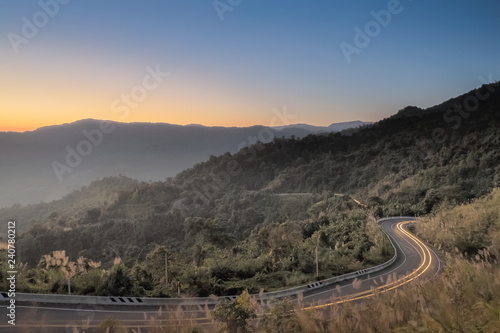 Mountain view morning of light-trails of many car on the road route 1148 around with mountain and colorful yellow sun light in the sky background, sunrise at Tham Sakoen View Point, Phayao, Thailand.