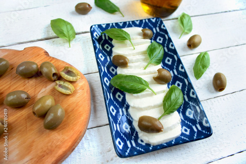 Mozzarella, green olives, basil leaves and a jug of olive oil
