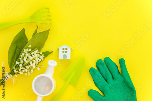 Flat Lay gardening tools, watering can, shovel, rake, glove, flowers and toy house on yellow colourful trendy background. Spring or summer in garden, eco, nature, farm, horticulture hobby concept photo