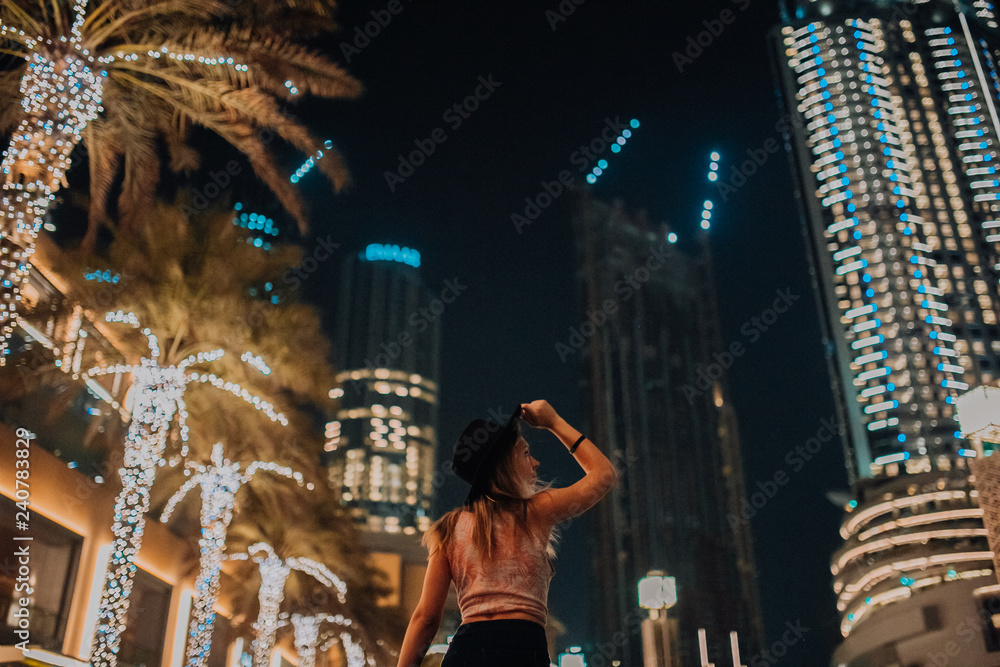 handsome women in hat fashionable clothes, brutal man, stylish outfit, walk down the street. cool light and palms in night city. Dubai