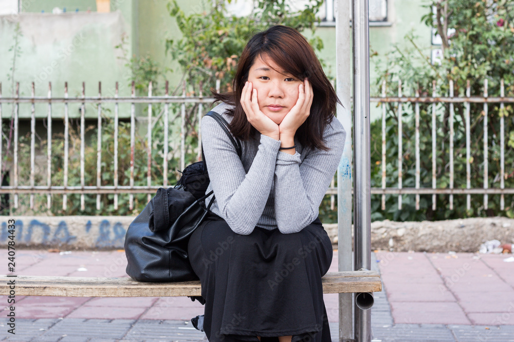 Fototapeta premium Chinese Girl Sitting on the Bench and Thinking While Waiting For Someone