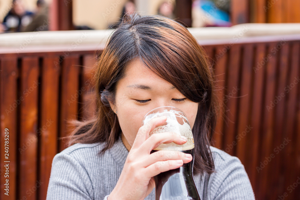 Chinese Girl Sitting in a Pub and Drinking Beer From the Glass