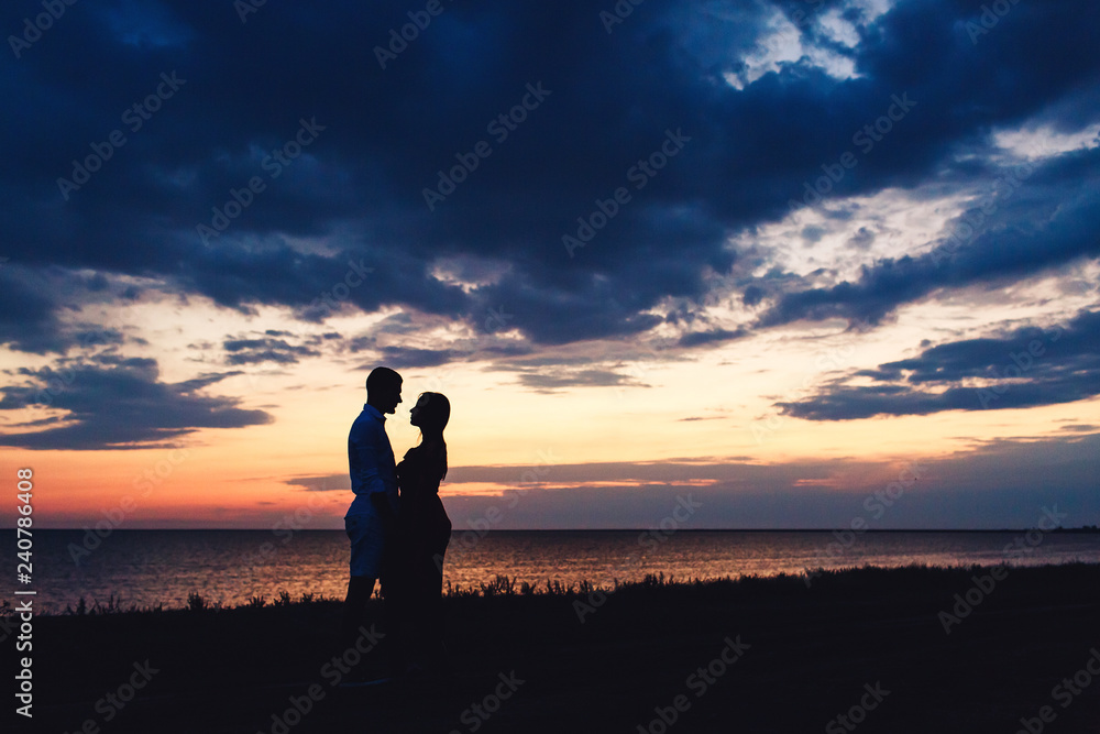 Silhouette photo of a couple in love on the background of a beautiful sunset sky and sea.