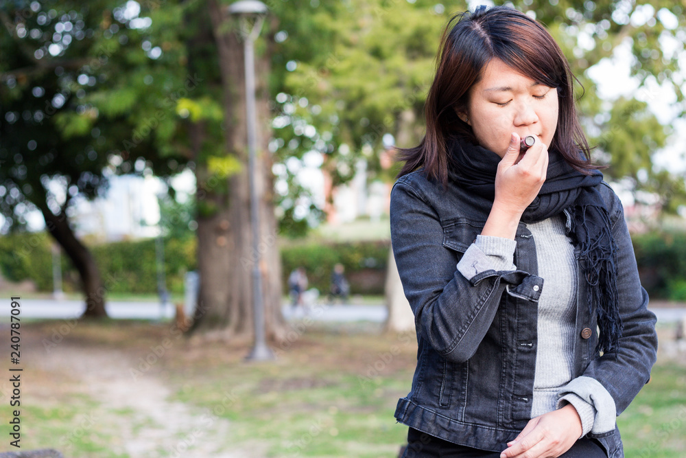 Chinese Girl in a Park Putting Lipstick on Her Lips Chinese Girl in a Park Putting Lipstick on Her Lips