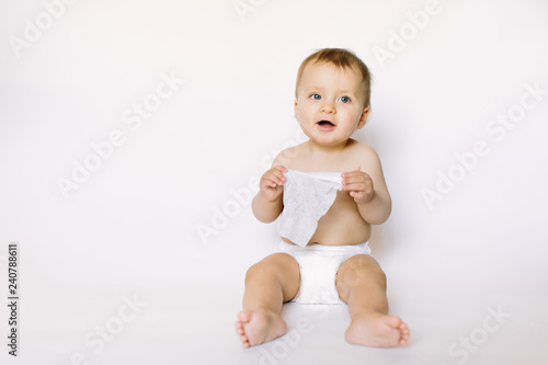 Slika na platnu Charming happy little baby girl in white diaper holding wet wipe in her hands and sitting isolated on white background