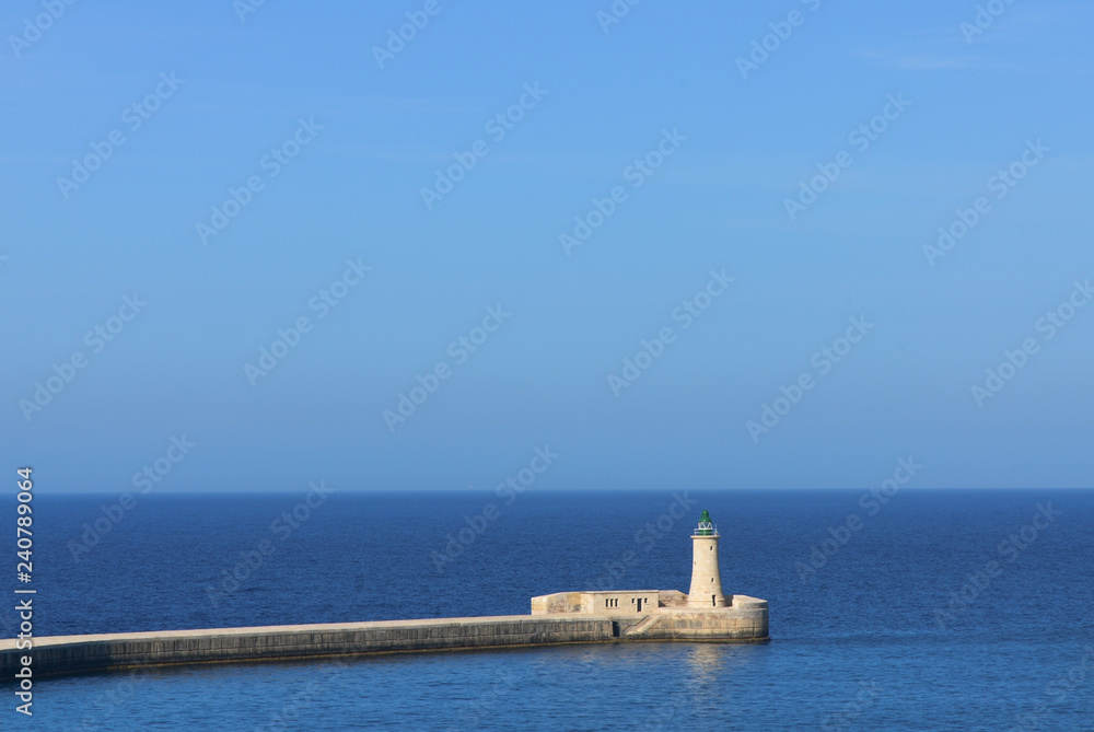 Harbour wall and lighthouse in Valletta against the blue Mediterranean Sea, Malta