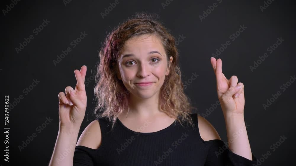 Portrait of charismatic caucasian girl with pink hair showing crossed fingers sign to show hope on black background. Portrait of charismatic caucasian girl with pink hair showing crossed fingers sign to show hope on black background.