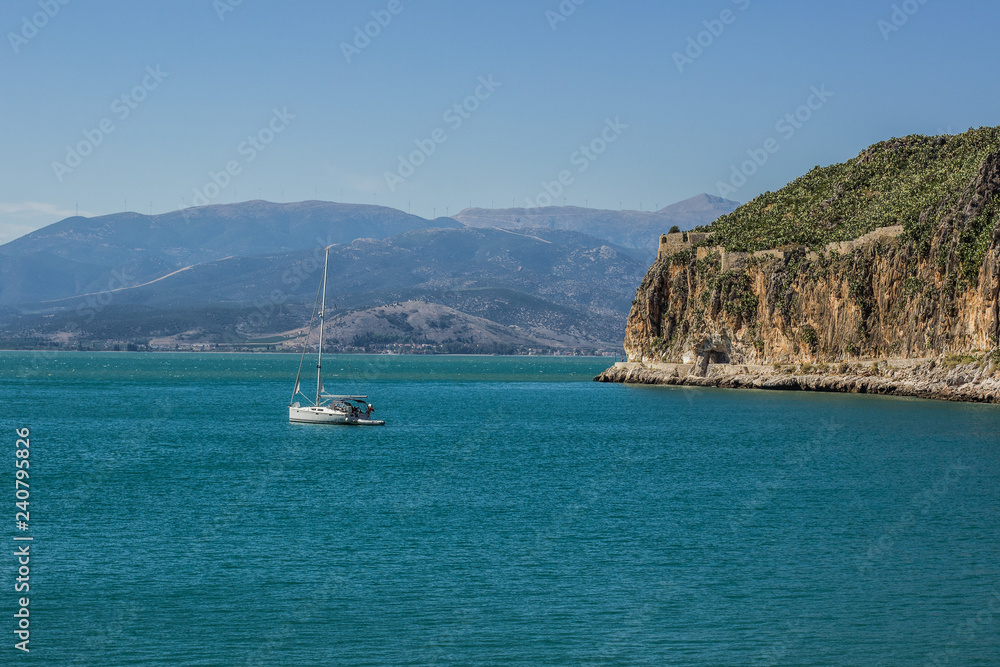 resort and vacation touristic concept of small white cruise ship in Mediterranean sea vivid blue water surface bay near  steep and high rock cape, tropic picturesque natural environment