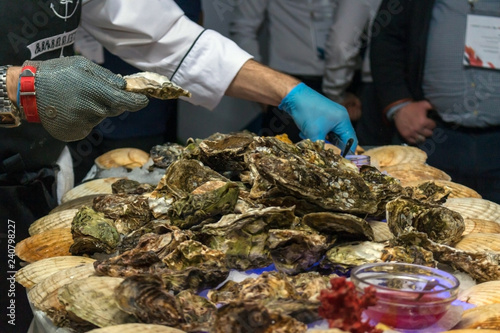 фотографія A man cleans oysters in shells with iron gloves.