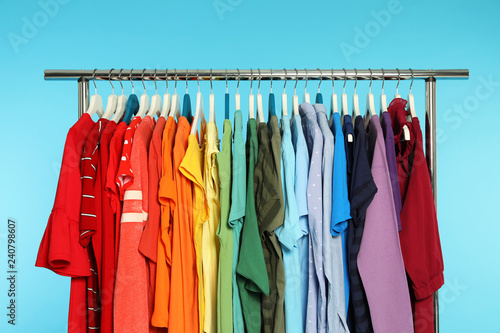 Wardrobe rack with different bright clothes on color background