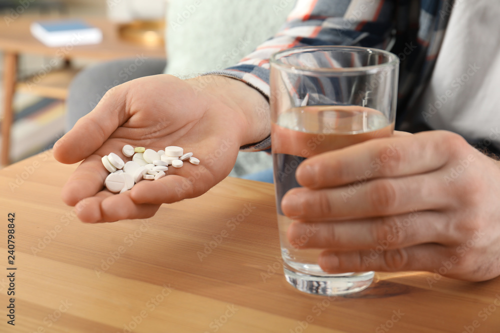 Man holding many pills and glass of water at table, closeup Man holding many pills and glass of water at table, closeup