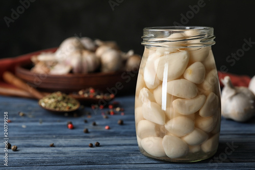 Preserved garlic in glass jar on wooden table. Space for text