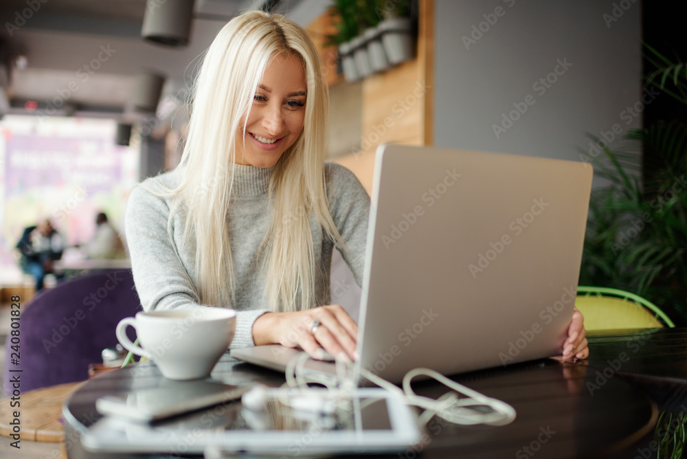 Confident young woman in casual wear working on laptop while sitting in creative office or cafe and woking. Holding a cup of coffee and smiling Confident young woman in casual wear working on laptop while sitting in creative office or cafe and woking. Holding a cup of coffee and smiling