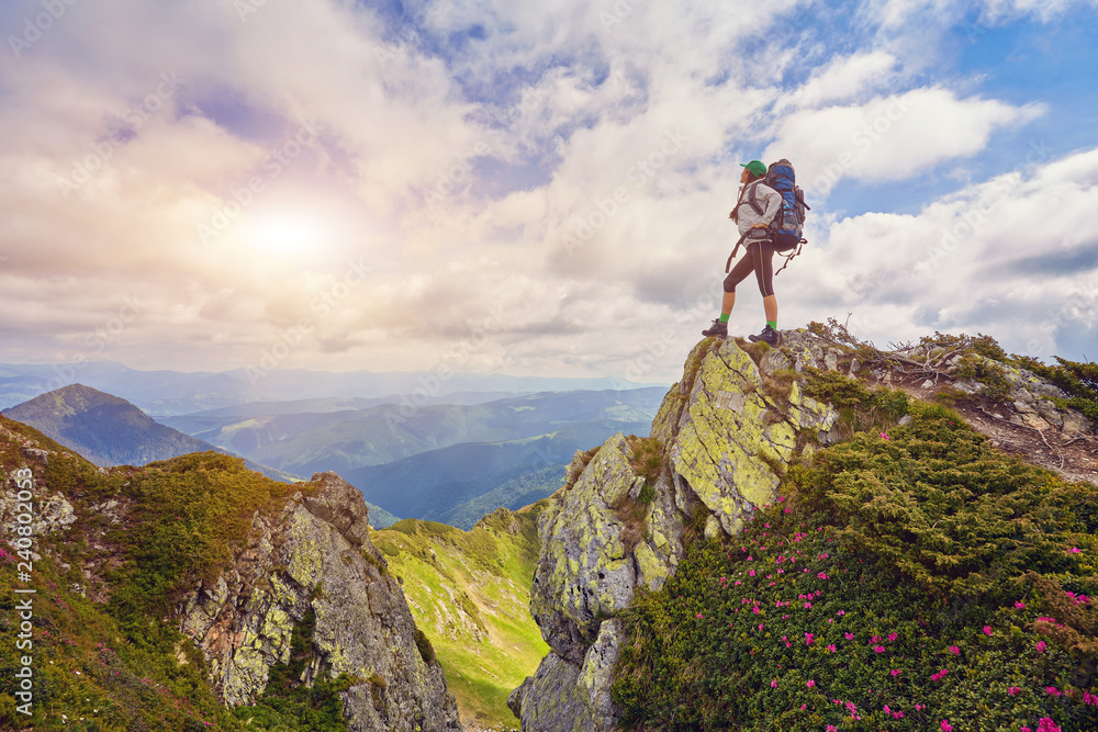 Lady hiker with backpack standing on top of the mountain