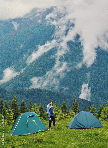 Hiker man standing near camping tent in carpathian mountains. Tourist enjoy mountain view.