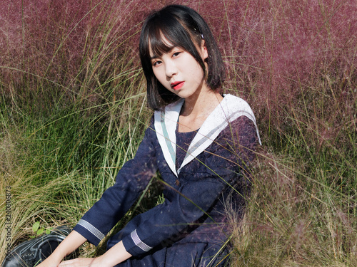 Outdoor portrait of beautiful young Chinese girl in blue school uniform japanese style sitting in pink hairawn muhly field, Cool girl, beauty, emotion, expression and people lifestyle concept. photo