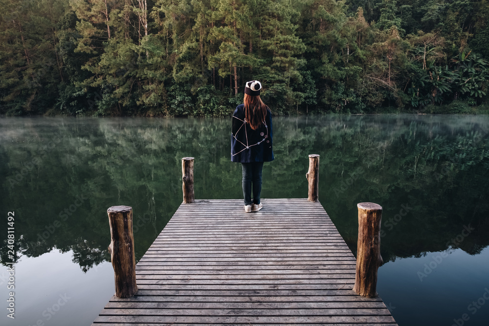 female Traveler sit on the Bamboo bridge beside the lake in the mist at morning sunrise at Pang Ung , Mae Hong Son province, Thailand