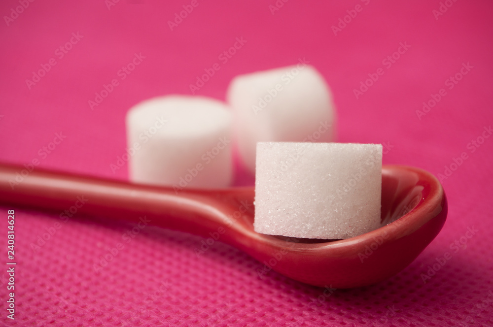 closeup of sugar in shaped circle in red spoon on pink background closeup of sugar in shaped circle in red spoon on pink background