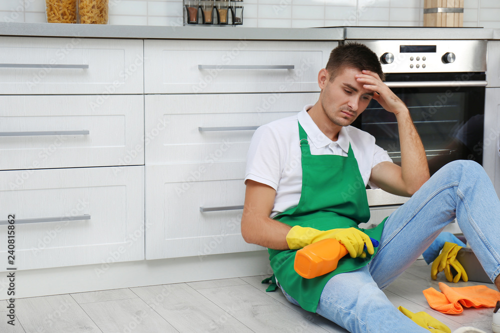 Exhausted janitor sitting on floor in kitchen, space for text. Cleaning service Exhausted janitor sitting on floor in kitchen, space for text. Cleaning service