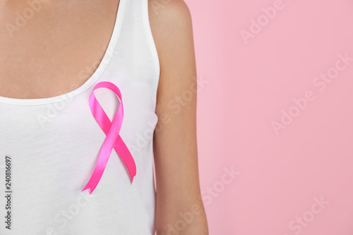 Woman with pink ribbon on color background, closeup with space for text. Breast cancer awareness