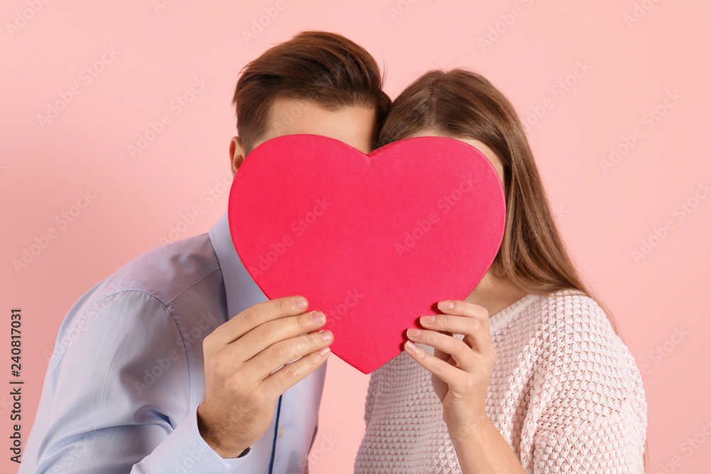 Man and woman hiding behind decorative heart on color background. Valentine's day Man and woman hiding behind decorative heart on color background. Valentine's day