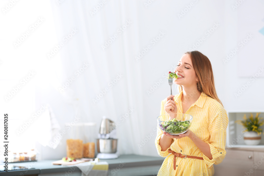 Happy young woman eating salad in kitchen, space for text. Healthy diet Happy young woman eating salad in kitchen, space for text. Healthy diet