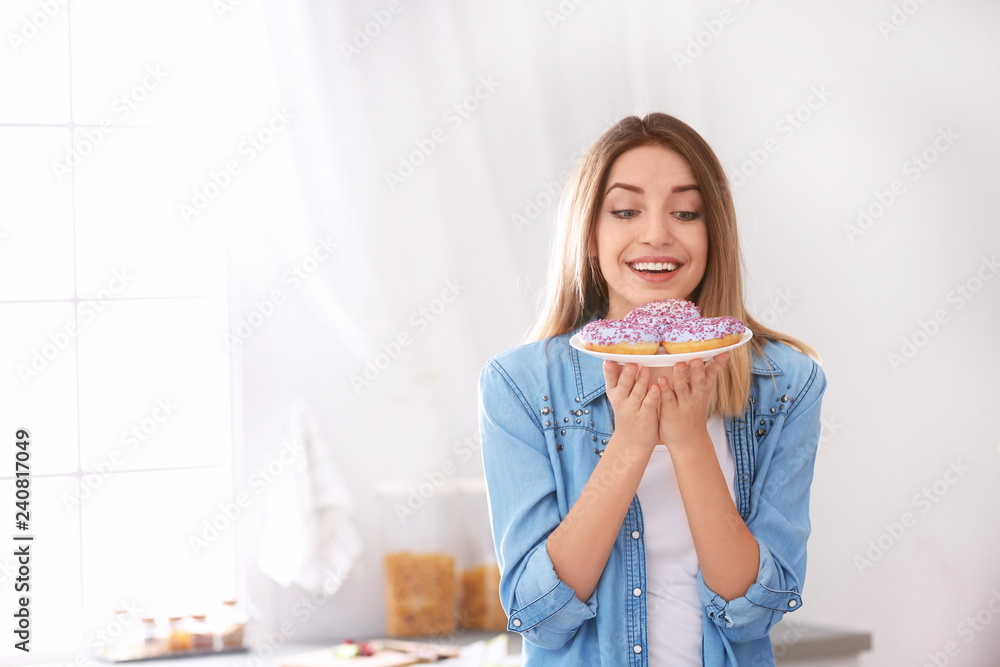 Beautiful young woman holding plate with donuts in kitchen, space for text. Failed diet Beautiful young woman holding plate with donuts in kitchen, space for text. Failed diet