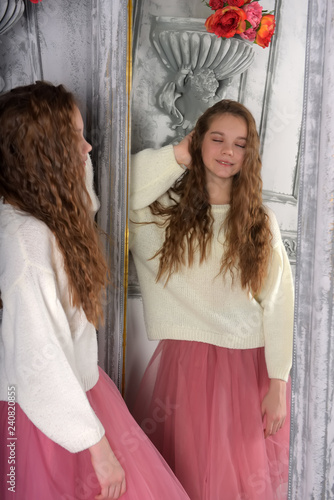 The girl looks in the mirror in a white sweater photo