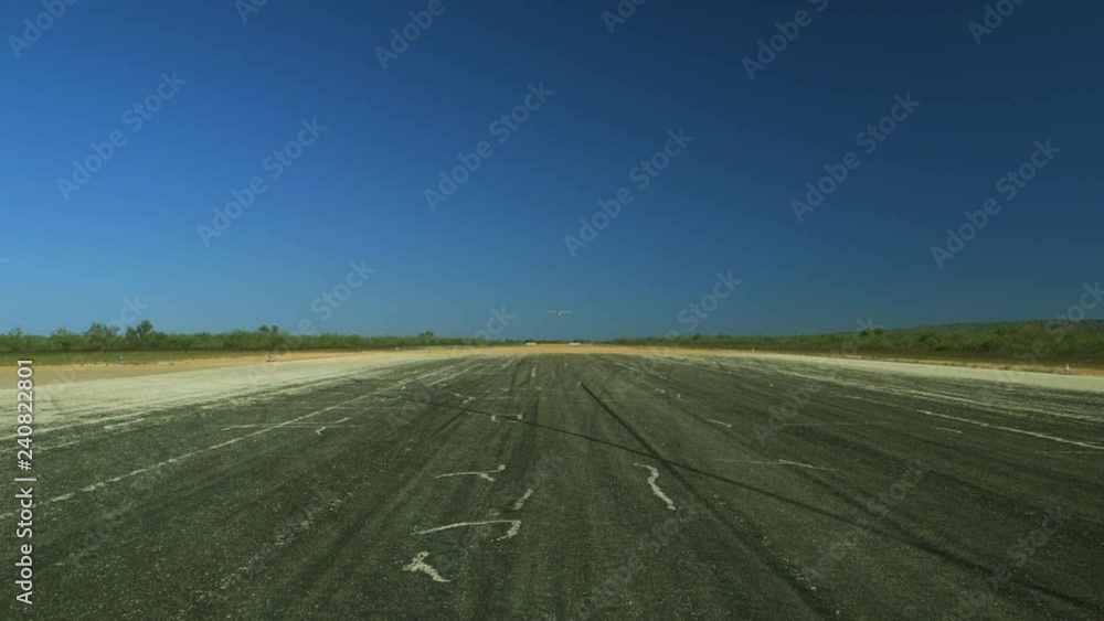 A long shot of a propeller plane flying over a runway as it descends to land, flying straight over the camera