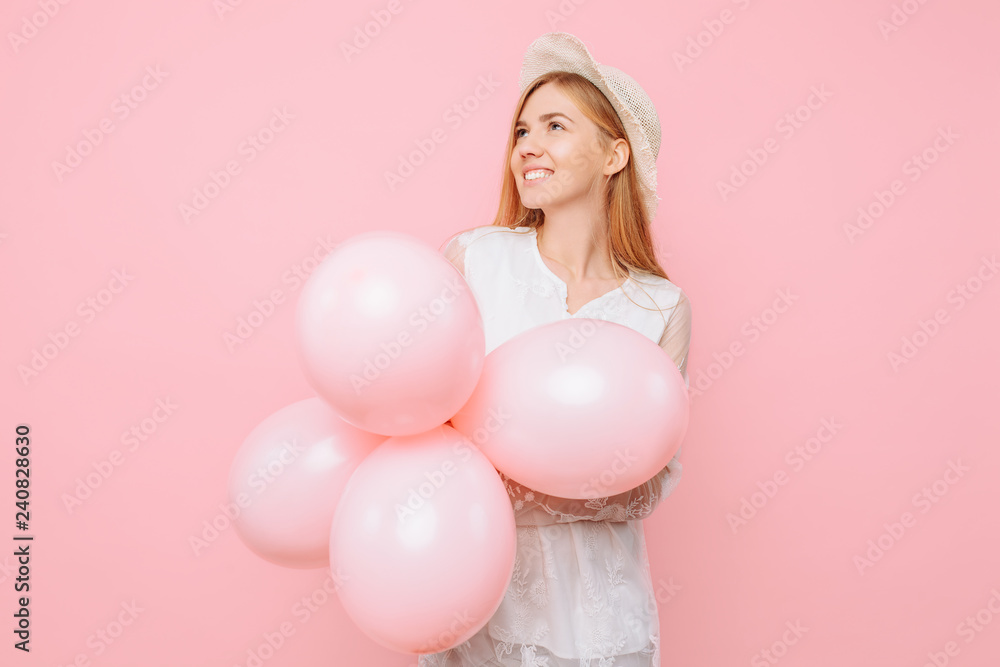 Happy thoughtful girl in a white dress, wearing a straw hat, holds balloons in her hands, on a pink background. March 8 concept Happy thoughtful girl in a white dress, wearing a straw hat, holds balloons in her hands, on a pink background. March 8 concept