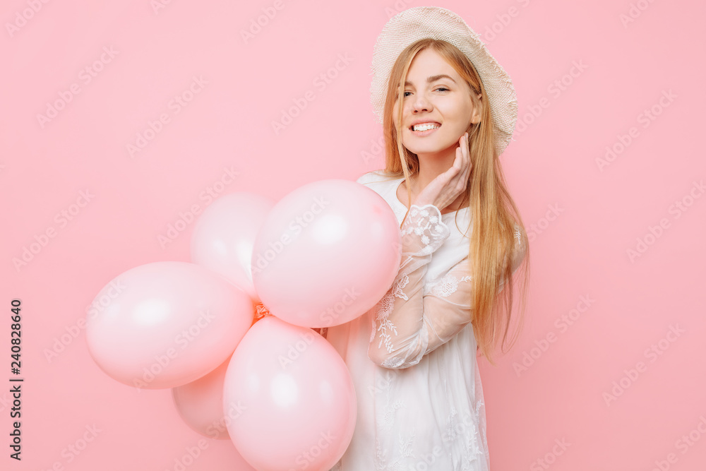 Happy girl in a white dress, in a straw hat, holds balloons in her hands, on a pink background. March 8 concept Happy girl in a white dress, in a straw hat, holds balloons in her hands, on a pink background. March 8 concept