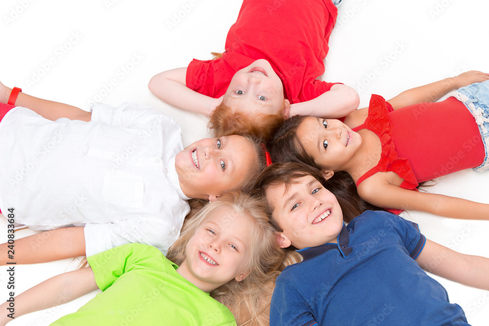 Close-up of happy children lying on floor in studio and looking up, isolated on white background, top view. Kids emotions and fashion concept