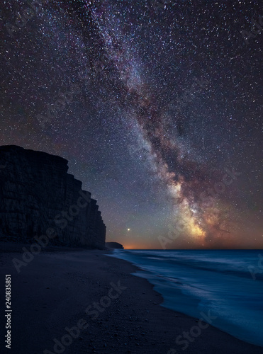 Vibrant Milky Way composite image over landscape of long exposure of West Bay in Dorset