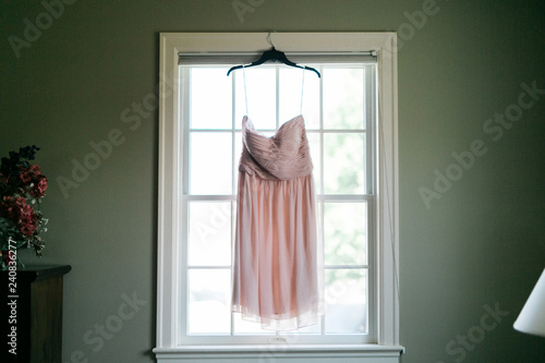 pink wedding dress hanging up near window