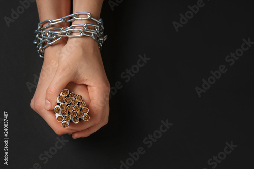 Female hands with chain and cigarettes on dark background. Concept of addiction