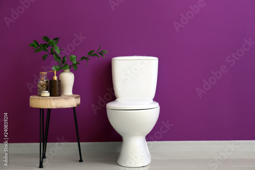 Modern ceramic toilet bowl near color wall in restroom