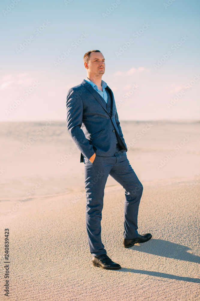 business-like, tall man in a strict, stylish, blue suit is standing and looking thoughtfully into the distance. Making serious decisions. Background white sands desert and sky. Fine art photo business-like, tall man in a strict, stylish, blue suit is standing and looking thoughtfully into the distance. Making serious decisions. Background white sands desert and sky. Fine art photo
